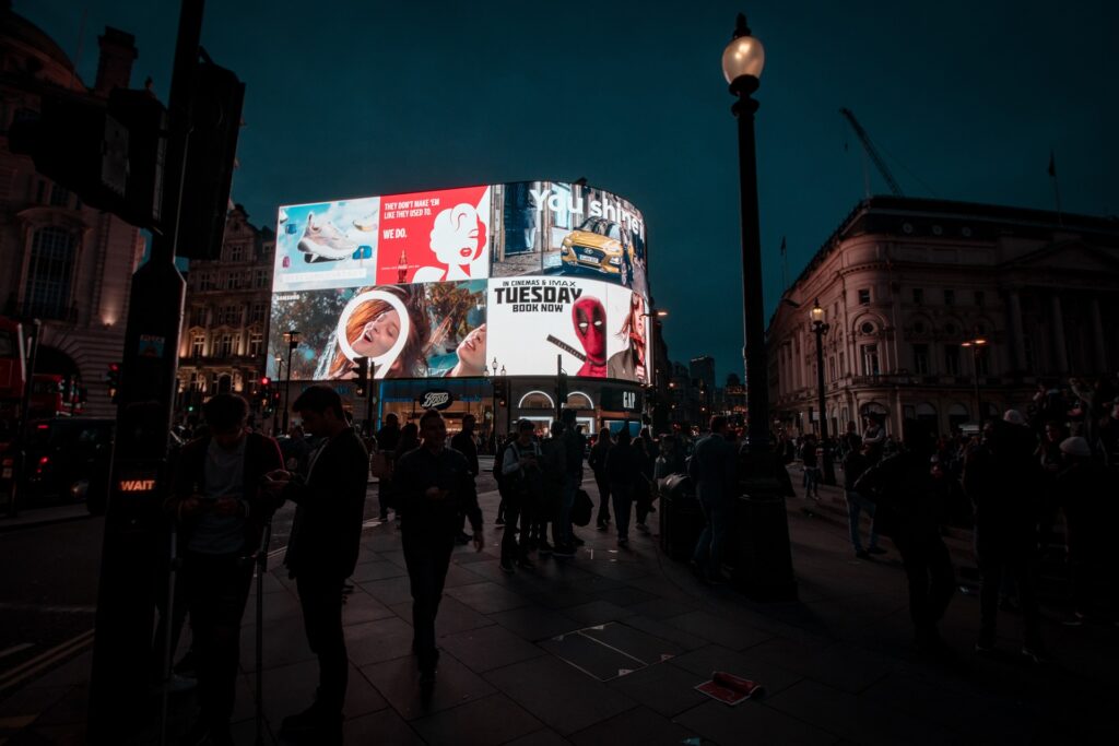 Pantallas digitales de publicidad exterior (DOOH) en una plaza urbana concurrida de noche, con anuncios luminosos y personas caminando alrededor